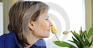 Middle-aged woman inhales yellow tulip scent. Flower fragrance, natural aromatherapy moment, Gen X. Flowers essence