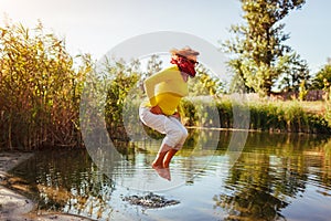 Middle-aged woman jumping on river bank on autumn day. Happy senior lady having fun walking in the forest