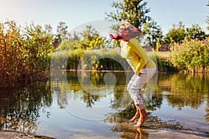 Middle-aged woman jumping on river bank on autumn day. Happy senior lady having fun walking in the forest