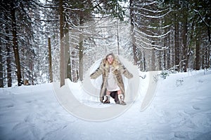 A middle-aged woman in a large warm fur coat and white angel wings in a winter forest with snow and snowdrifts. Fairy angel in a