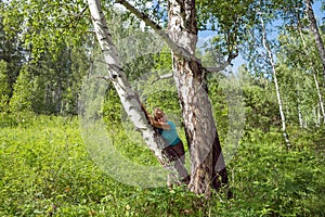 A middle-aged woman leaned against a birch tree in the forest.