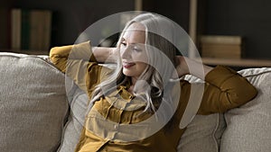 Middle-aged woman with long grey hair sit on cozy sofa