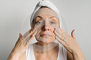 Middle-aged woman lookin in a mirror and checking bags under the eyes, skin and wrinkles. Skincare, cosmetology concept