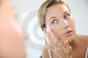Middle-aged woman looking at the mirror and nourishing her skin