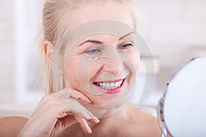 Middle aged woman looking at wrinkles in mirror. Plastic surgery and collagen injections. Makeup. Macro face. Selective