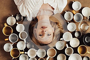 A middle aged woman looks into the camera and there are many empty cups on the floor. The concept of deadline, nervous exhaustion