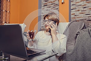 Middle aged woman making call and using laptop at home