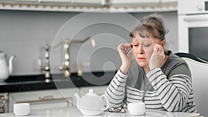 Middle aged woman massaging temple having headache in kitchen at home