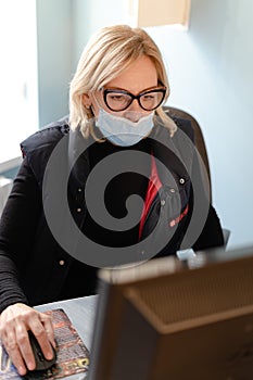 Middle aged woman with medical mask working with pc computer. Small business owner on quarantine