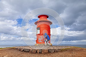 middle aged woman photographer take a shot with camera in front of a red lighthouse