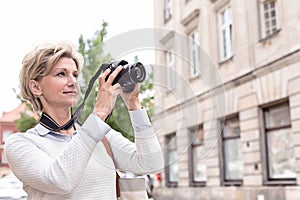 Middle-aged woman photographing through digital camera in city