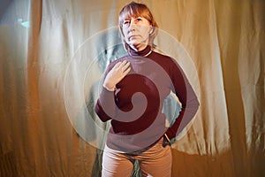 A middle-aged woman poses showing clothes against a background of green crumpled curtains. An inept model in an inept shoot photo