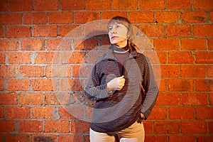 A middle-aged woman poses showing clothes near red brick wall. An inept model in an inept shoot