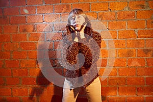 A middle-aged woman poses showing clothes near red brick wall. An inept model in an inept shoot