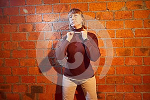 A middle-aged woman poses showing clothes near red brick wall. An inept model in an inept shoot