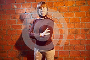 A middle-aged woman poses showing clothes near red brick wall. An inept model in an inept shoot