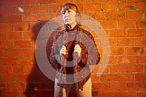A middle-aged woman poses showing clothes near red brick wall. An inept model in an inept shoot photo