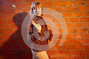 A middle-aged woman poses showing clothes near red brick wall. An inept model in an inept shoot photo