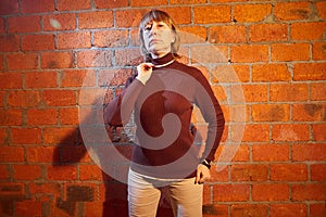 A middle-aged woman poses showing clothes near red brick wall. An inept model in an inept shoot photo