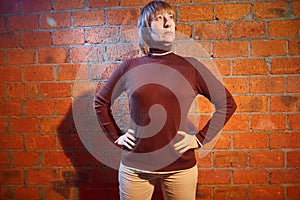 A middle-aged woman poses showing clothes near red brick wall. An inept model in an inept shoot photo