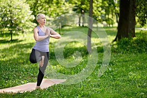 Middle aged woman practicing yoga outdoors in tree pose.Going in for sports in the city park.