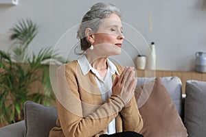 Middle aged woman praying, eyes closed, looking up, hoping for best, asking for forgiveness