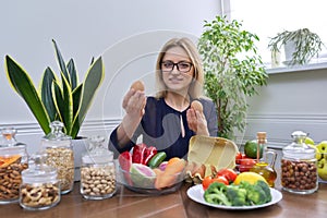 Middle aged woman professional nutritionist sitting at table with foods, eggs