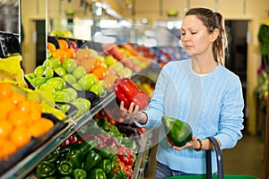 Middle-aged woman purchaser holding pepper in grocery store