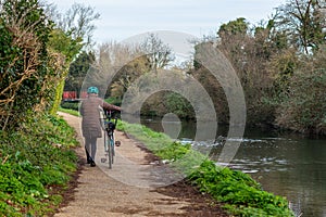 A middle aged woman push a bicycle along a canal towpath