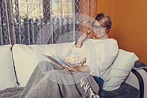 Middle aged woman reading book and eating popcorn