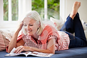 Middle Aged Woman Reading Magazine Lying On Sofa