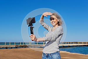 Middle-aged woman recording video on smartphone with outdoor on seashore