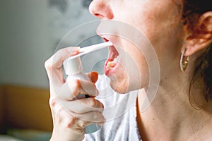 Middle-aged woman. With red hair. With a tired, sickly face. Sprays a spray for sore throat. On a gray background