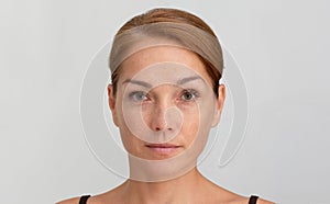 Middle aged woman with reddish hair and calm look looking at camera on grey background