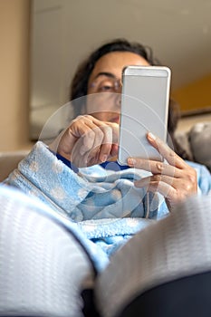 Middle-aged woman relaxing at home on the sofa reading her text messages on her mobile phone