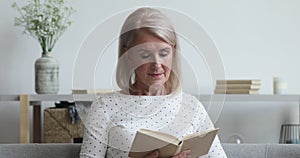 Middle aged woman relaxing reading book sit on sofa