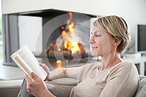 Middle-aged woman relaxing on the sofa reading book