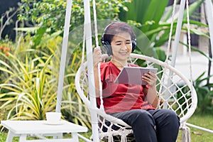 Middle aged woman relaxing on swing listen music on the tablet computer in backyard