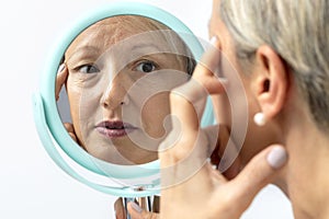 Middle aged woman reviewing wrinkles in hand mirror