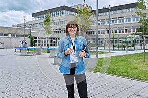Middle-aged woman school teacher with digital tablet posing near school building