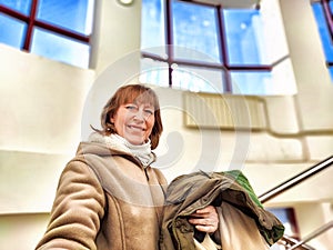 Middle-Aged Woman Shopping Second-Hand Clothes in Store. Smiling woman holding eco-friendly second-hand garments