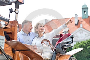 Middle-aged woman showing something to man while sitting in horse cart