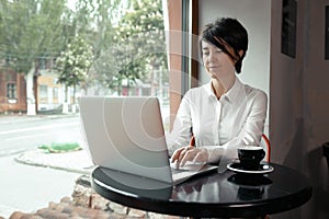 A middle aged woman sits in a cafe and works at a laptop