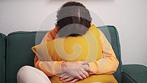 middle-aged woman sits at home on a sofa in depression, hugs a pillow and covers face.