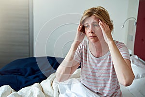 A middle-aged woman is sitting on the bed, holding her head.