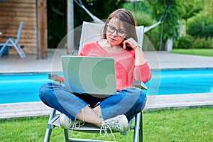 Middle aged woman sitting in chair in backyard with laptop