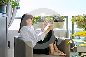 Middle-aged woman sitting at home in chair using digital tablet