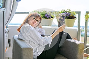 Middle-aged woman sitting at home in chair using digital tablet