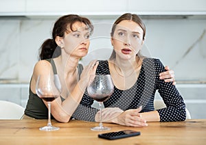 Middle-aged woman sitting at table while another woman trying to calm her sitting by her side