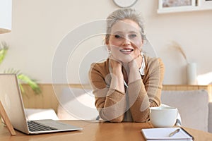Middle aged woman sitting at a table with a laptop and looking at the camera smiling